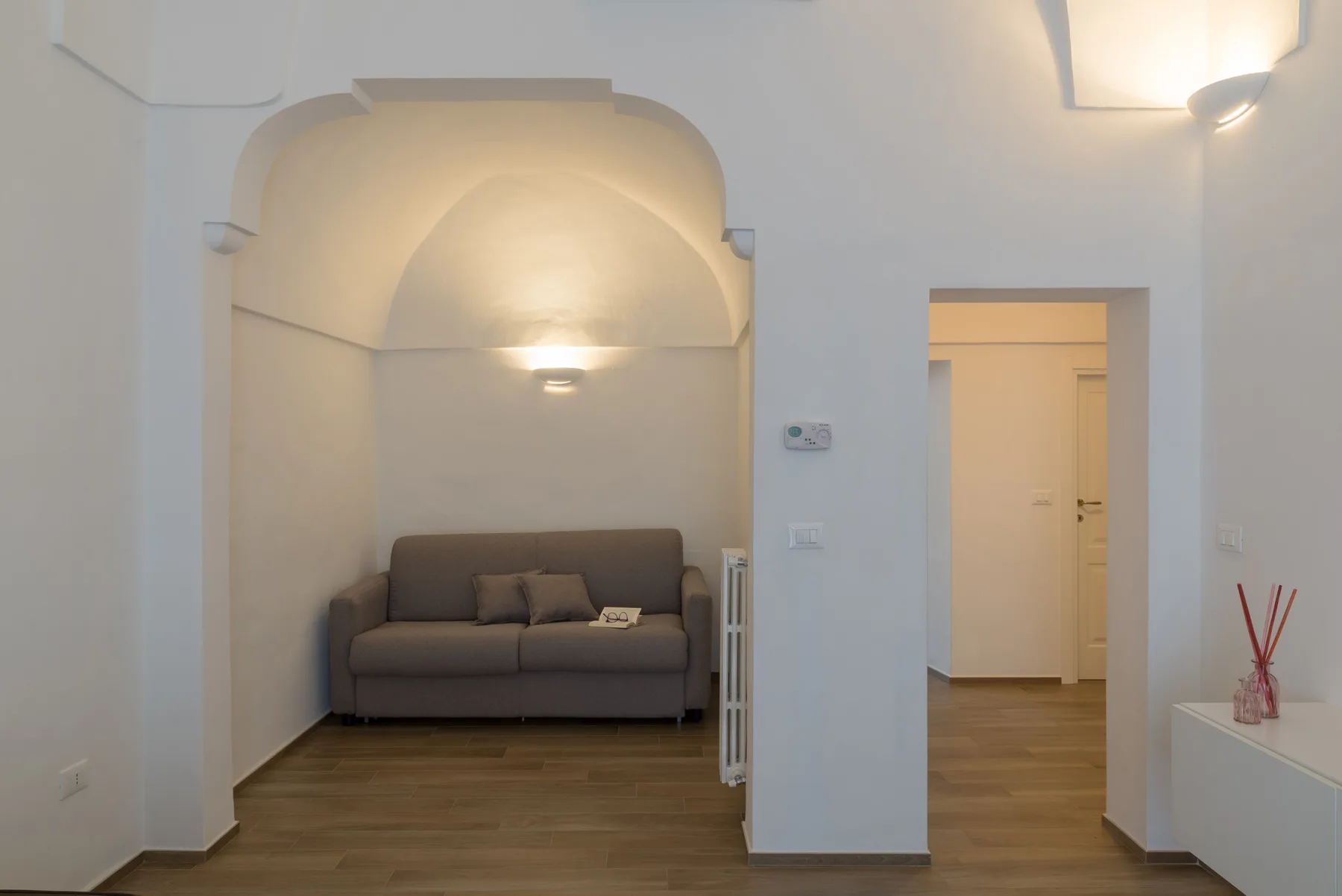 Una sala de estar con asientos bajo un arco, junto a una puerta abierta.