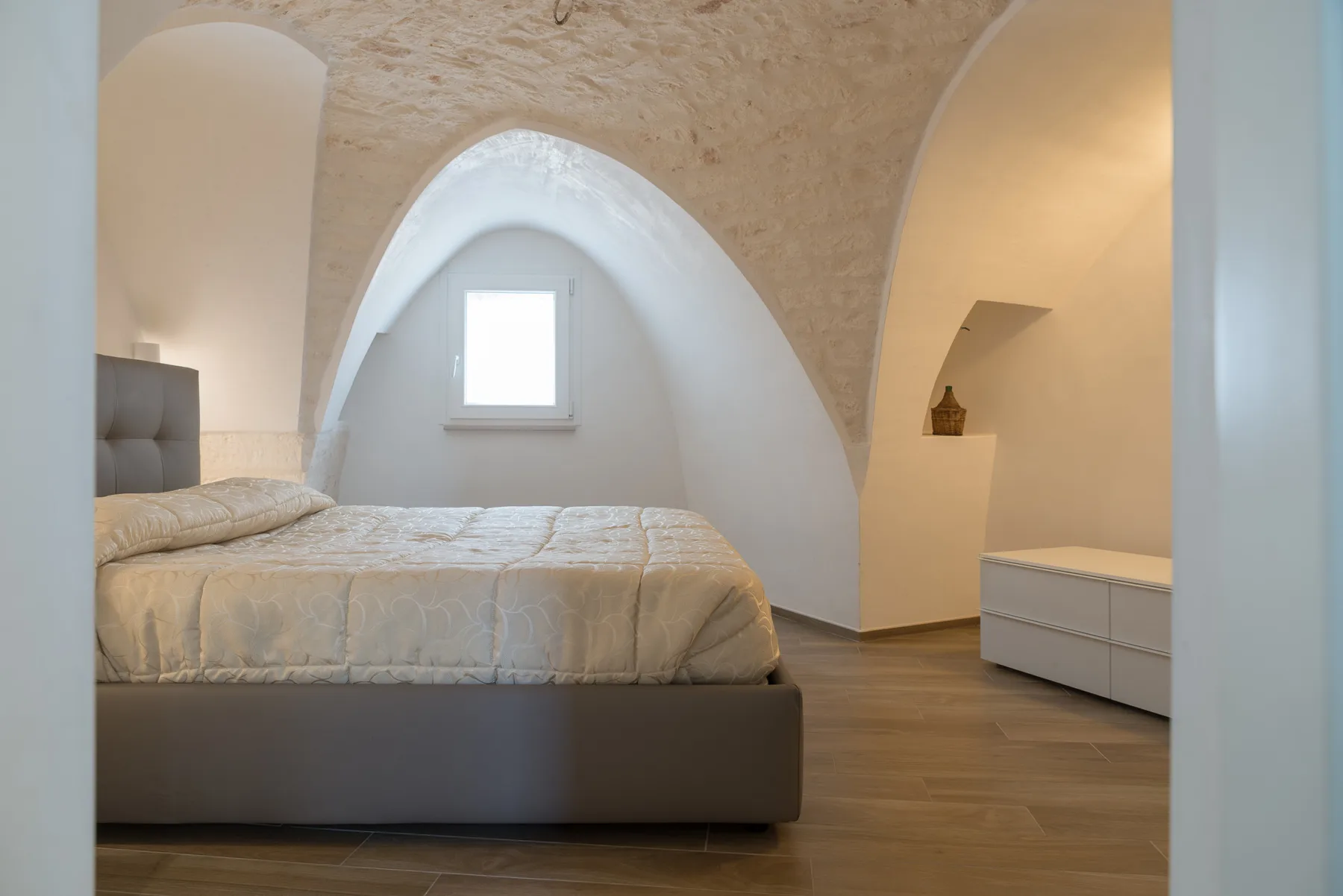 Un dormitorio con una cama bajo arcos de yeso curvos y una ventana pequeña.