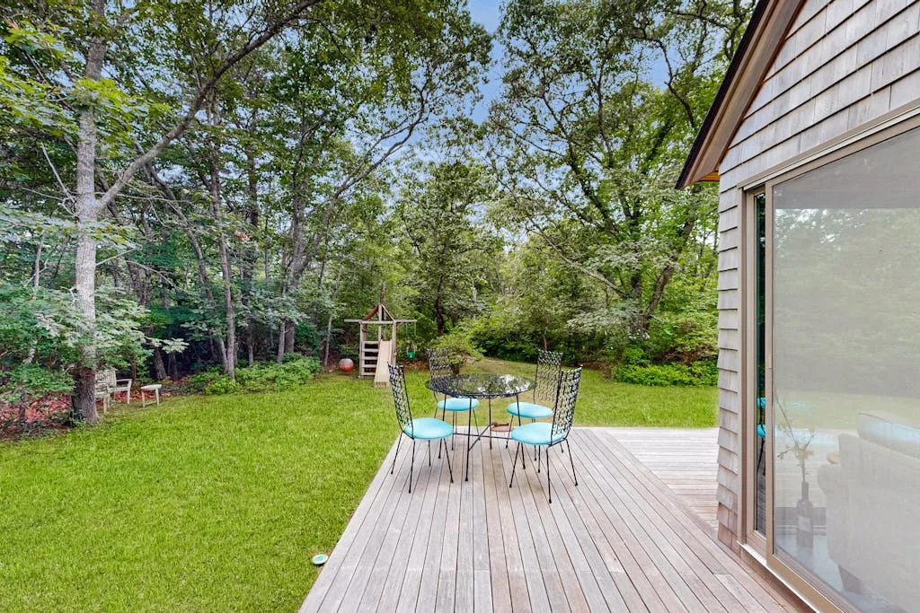 Una terraza de madera con asientos al aire libre da a un césped y árboles.