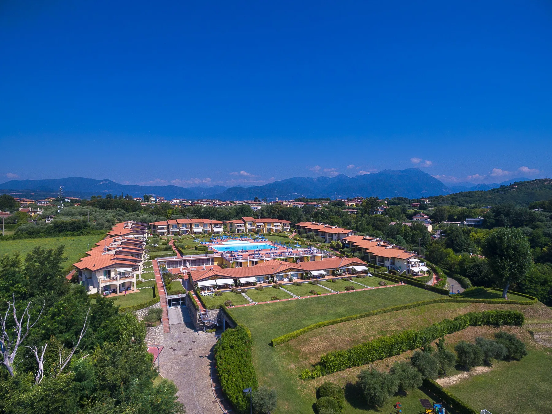 An aerial view shows a resort complex with buildings, a pool, and surrounding greenery.