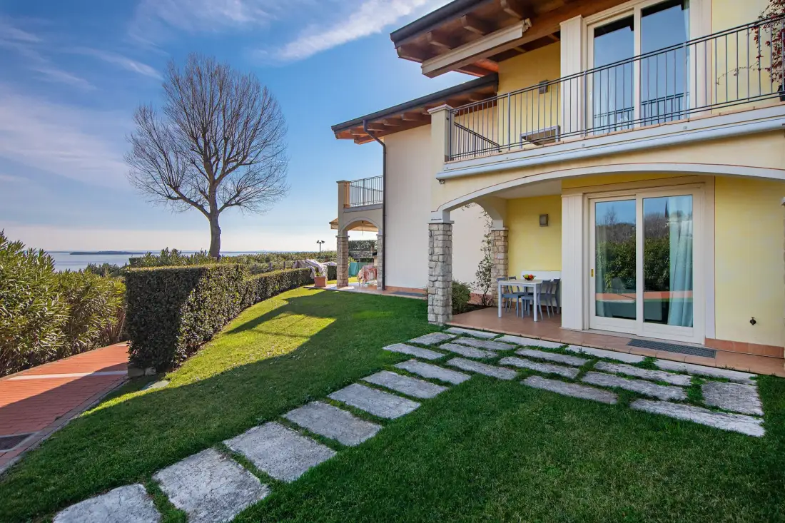 A two-story house opens onto a lawn with a stone path and outdoor seating.