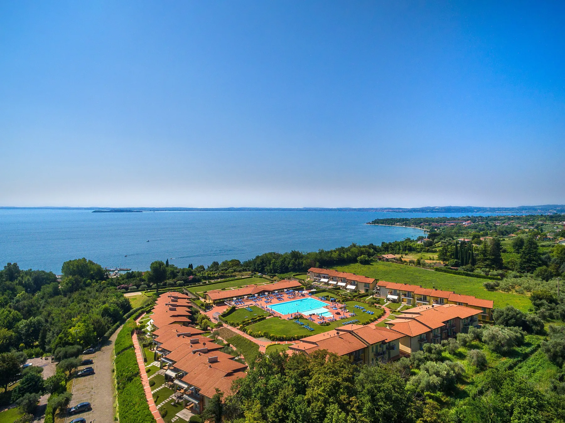A coastal resort complex with orange roofs surrounds a bright blue swimming pool.
