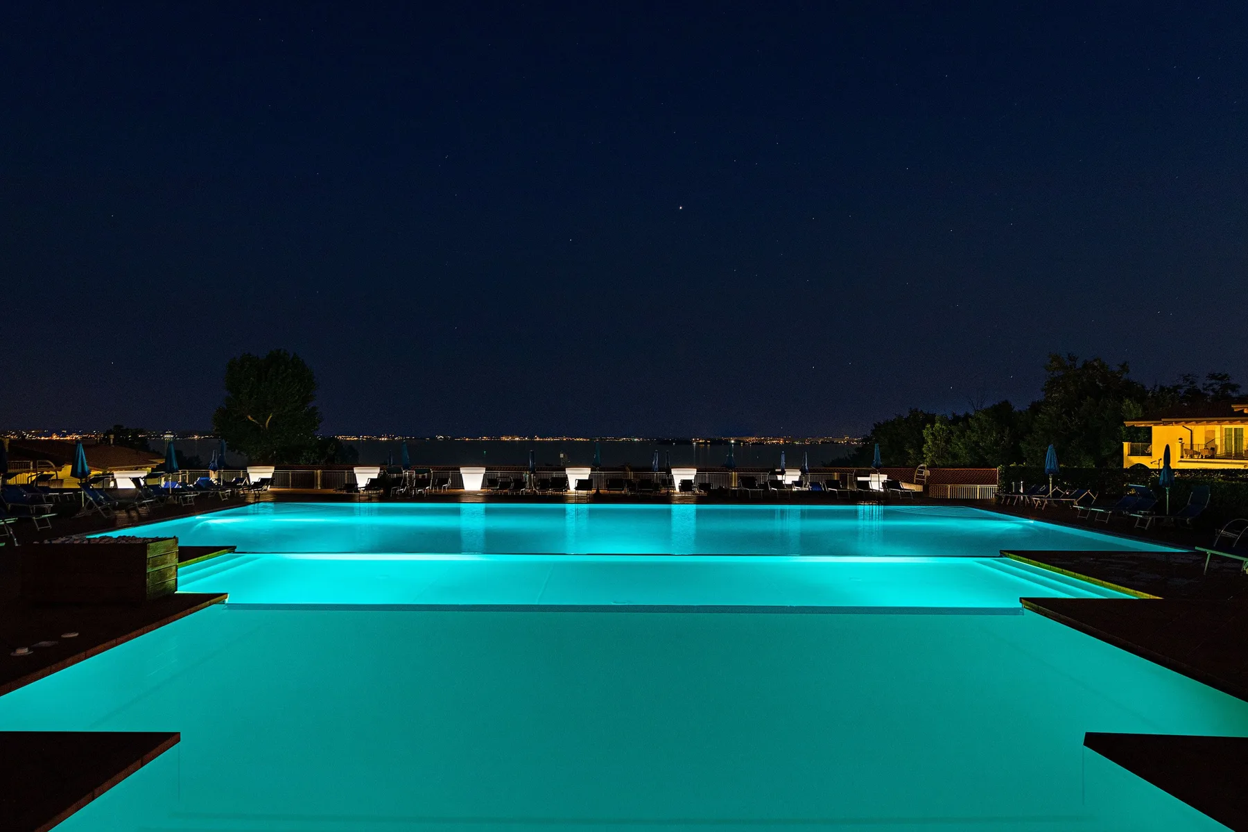 An outdoor swimming pool glows turquoise at night beneath the dark sky.