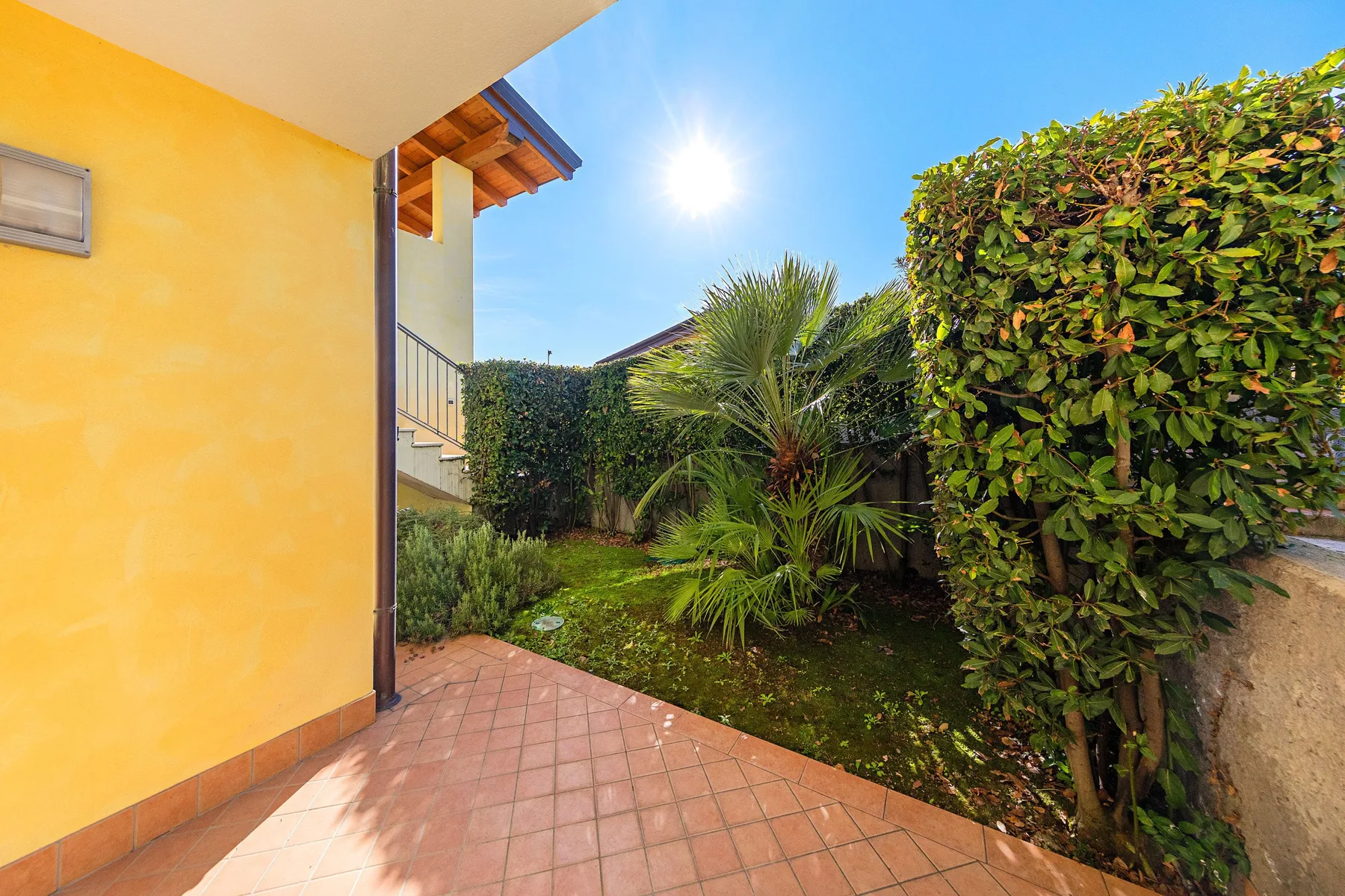 A tiled patio beside a yellow exterior wall, with dense garden greenery.