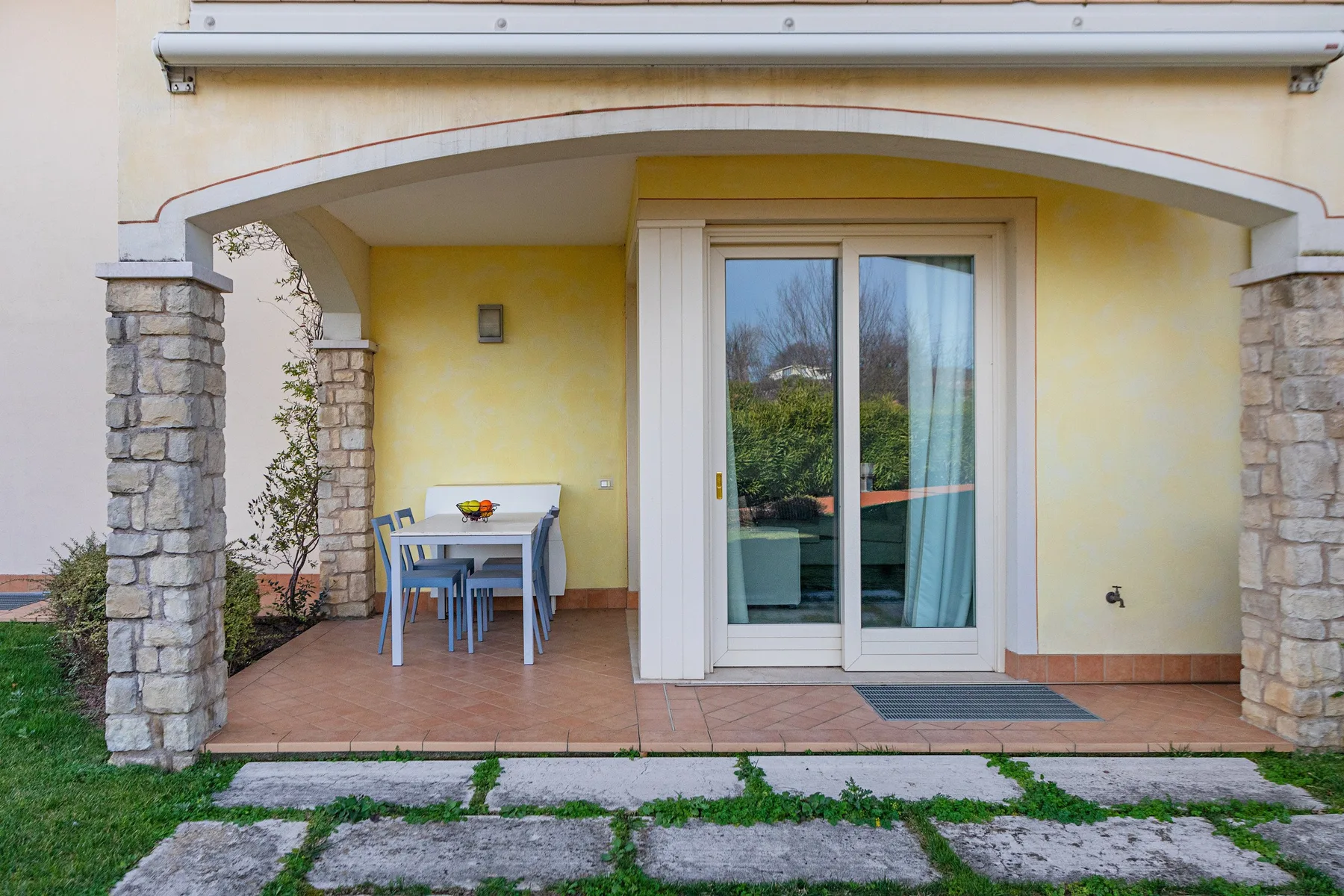 A covered patio with a table and sliding glass doors opening onto a garden.