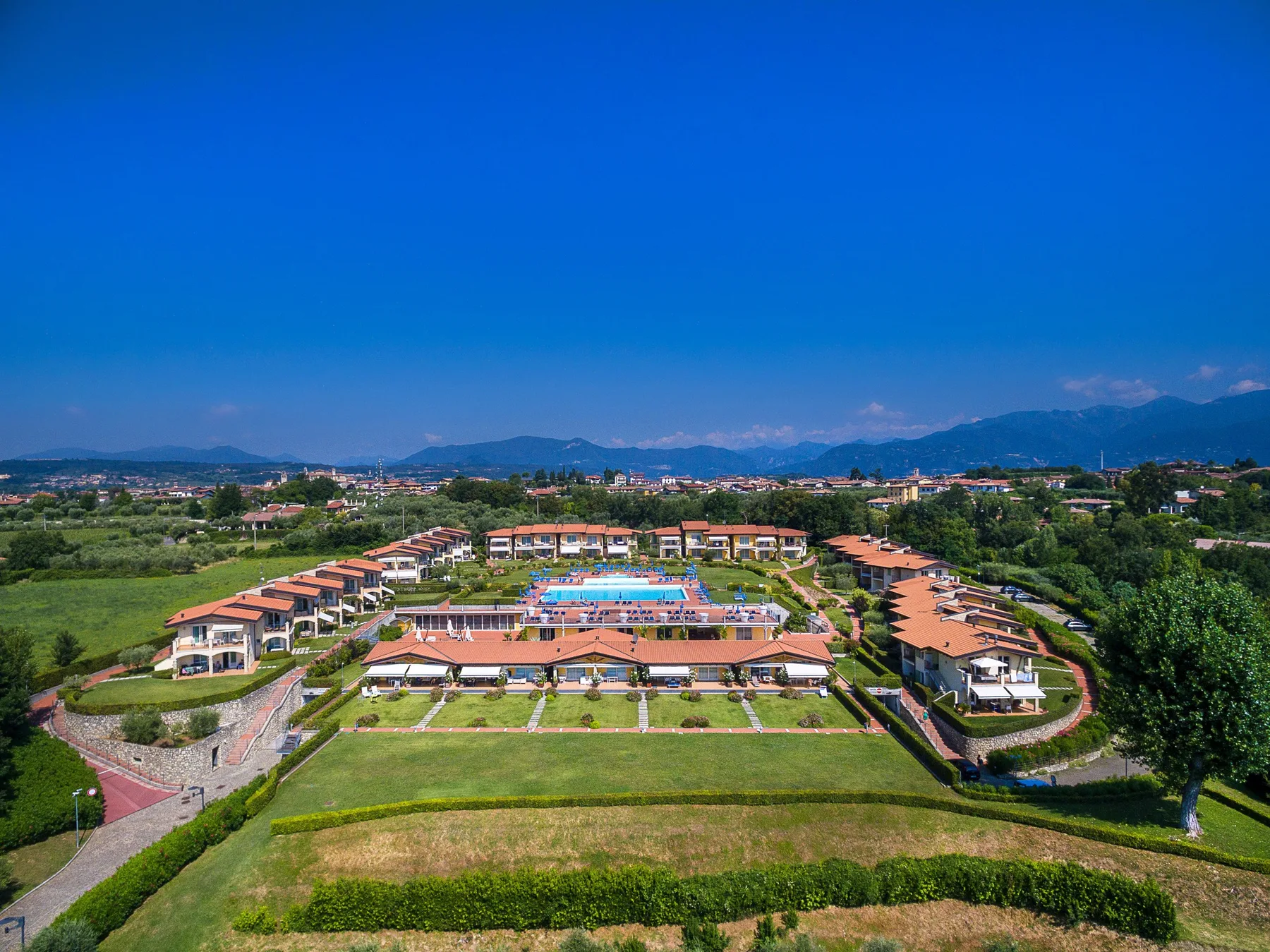 Aerial view of a resort complex with rows of buildings and a central swimming pool.