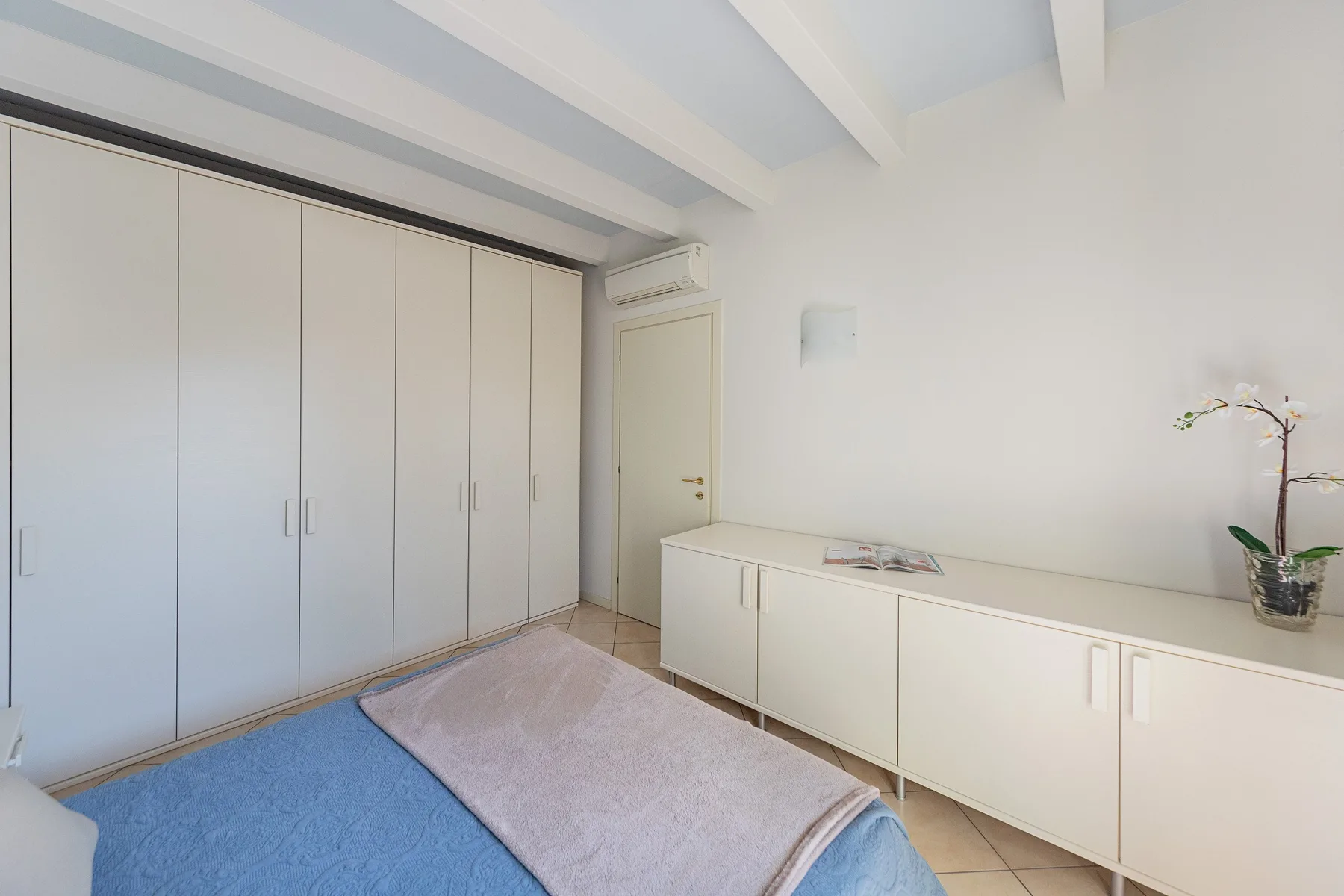 A bedroom with a bed, built-in wardrobes, and a long low cabinet.