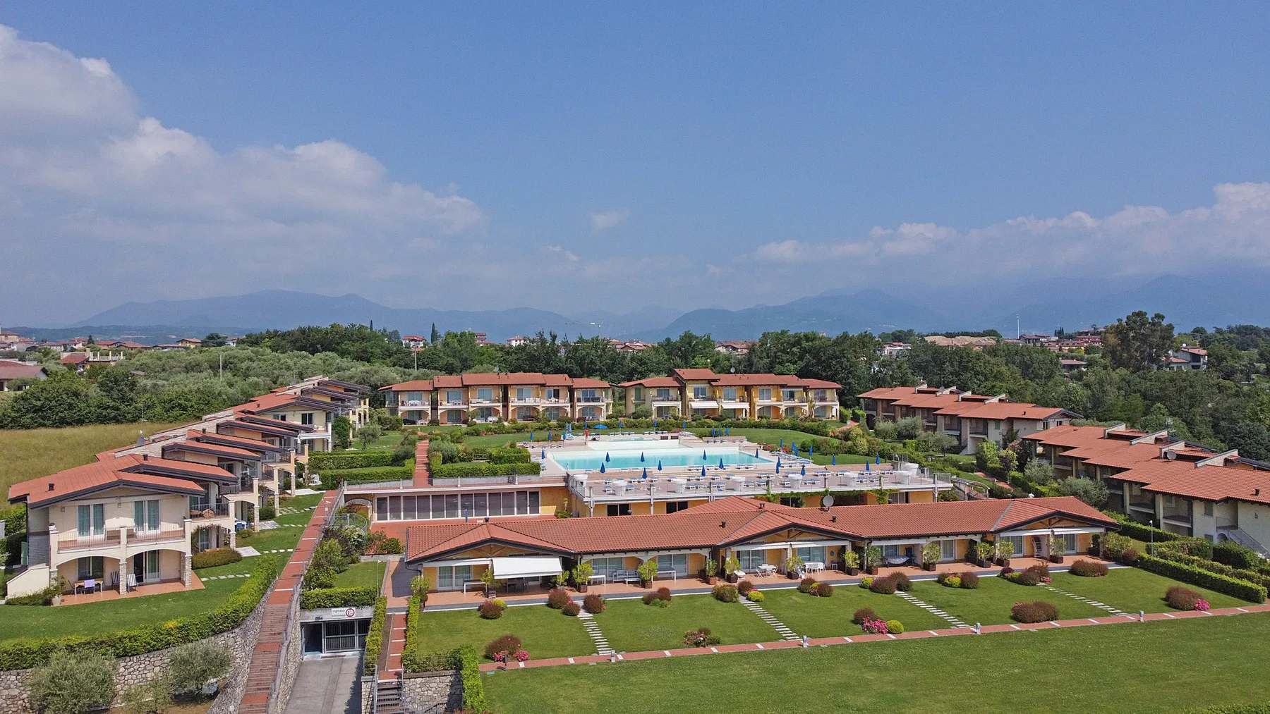 A resort complex with red-tiled buildings surrounds a central swimming pool.