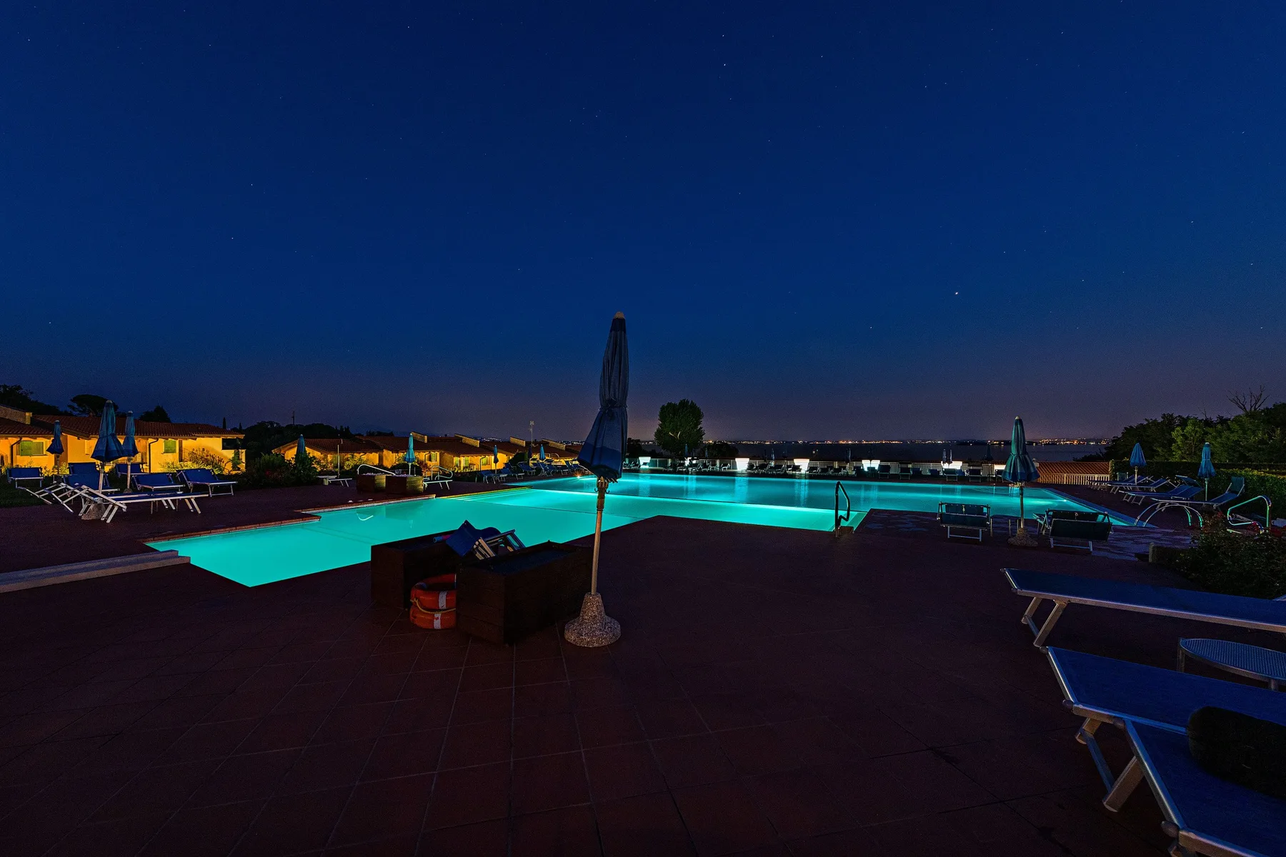 A swimming pool glows beside lounge seating on a terrace at night.