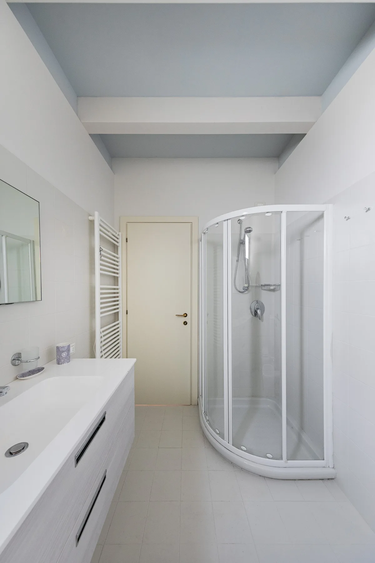 A bright bathroom with a sink, mirror, and curved glass shower.