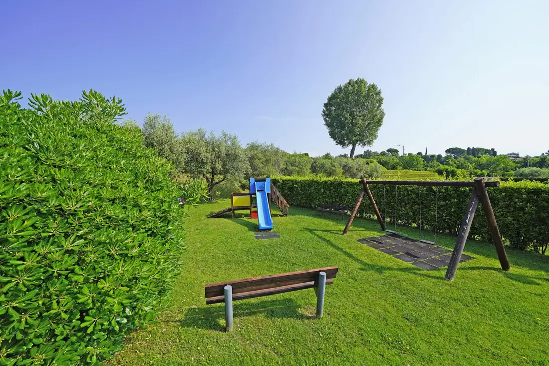 A grassy outdoor play area with a slide, swings, and a bench.