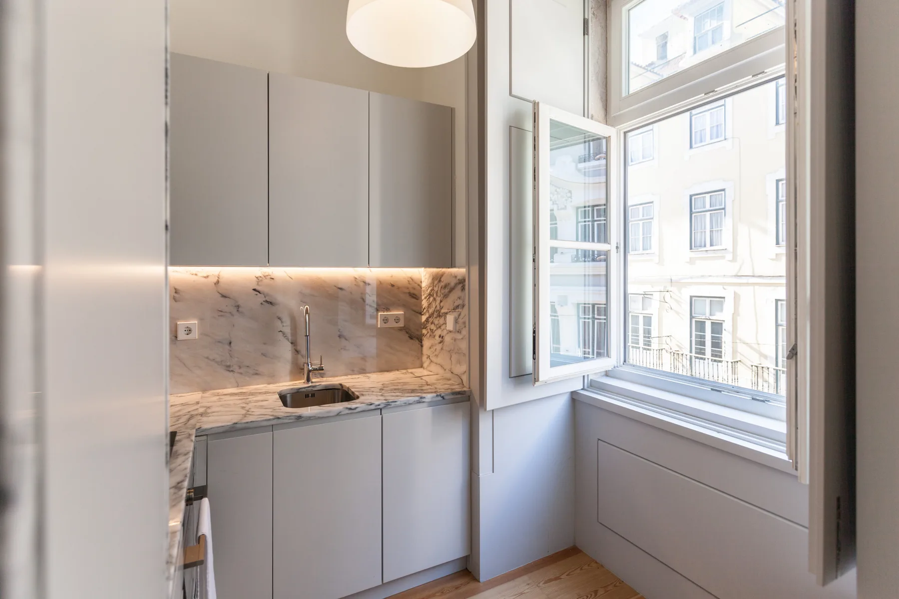 A modern kitchen with light cabinets, a stone backsplash, and an open window.