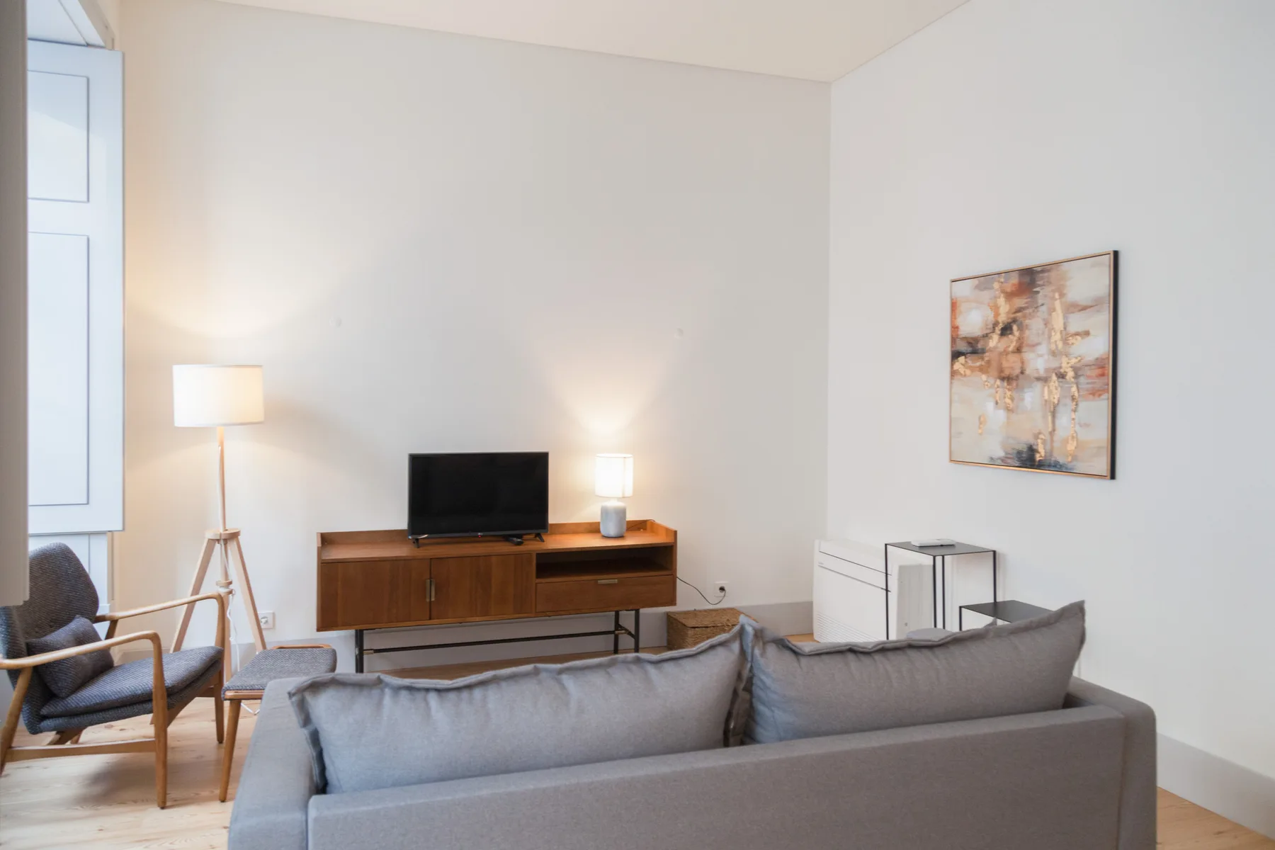 A living room with gray seating, a television, and a framed abstract painting.