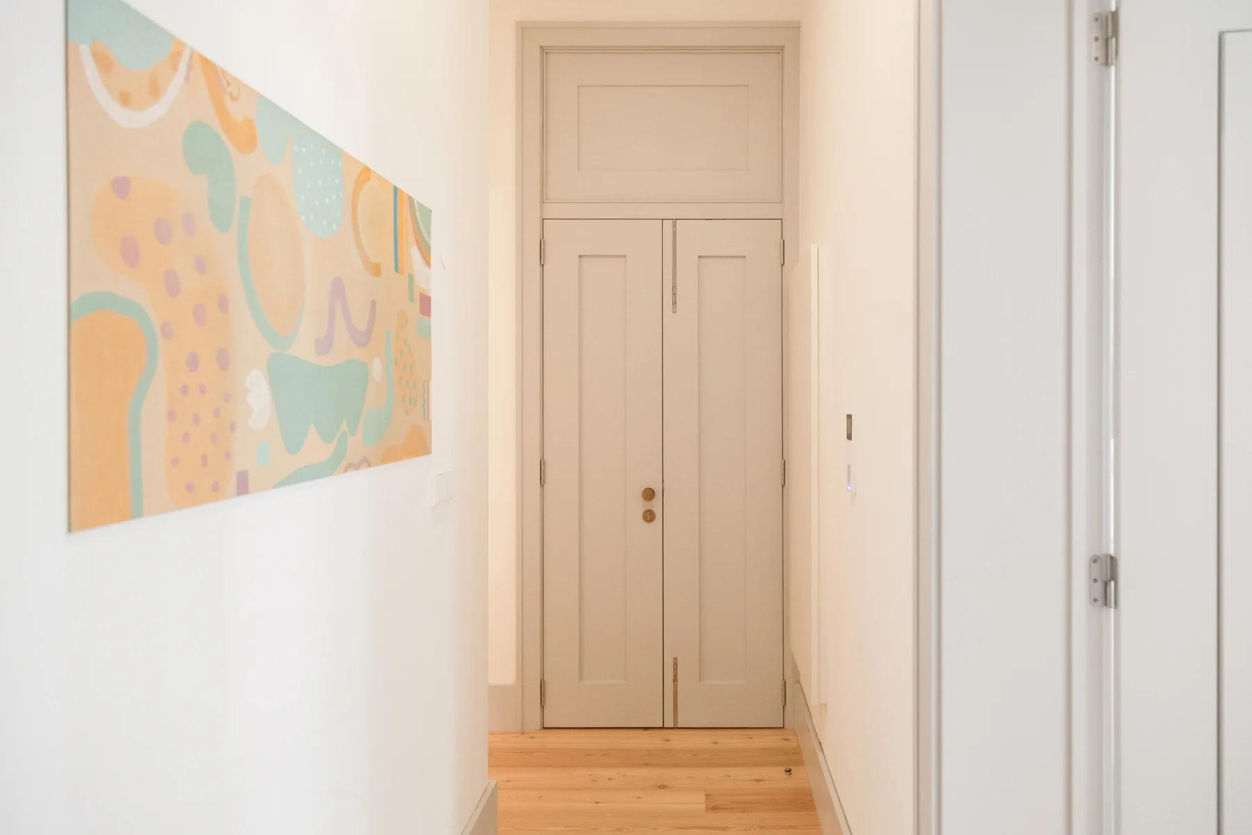 A bright hallway with pale wood flooring and an abstract wall painting.