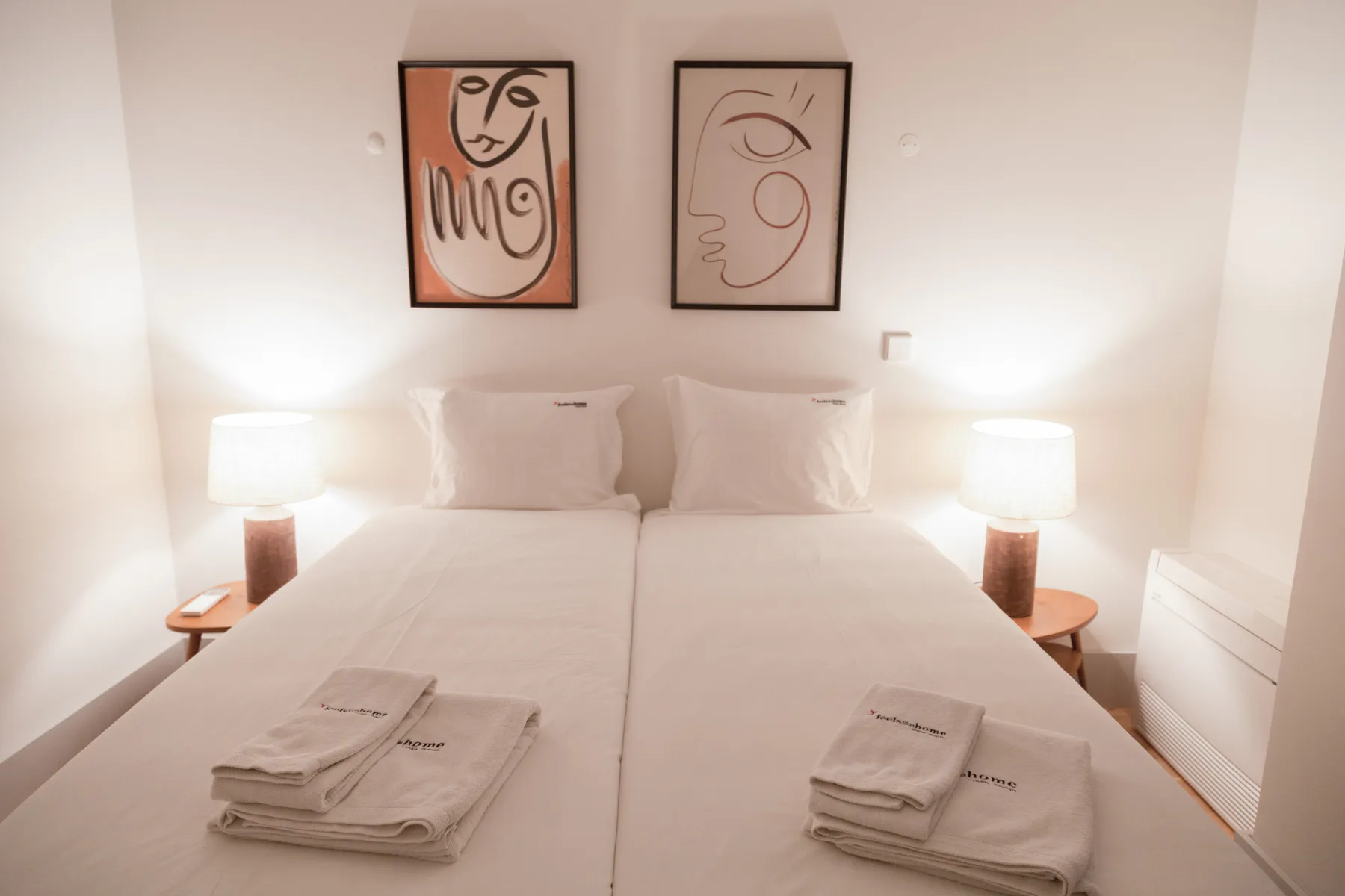 A bedroom with two beds, bedside lamps, and framed artwork above the headboards.