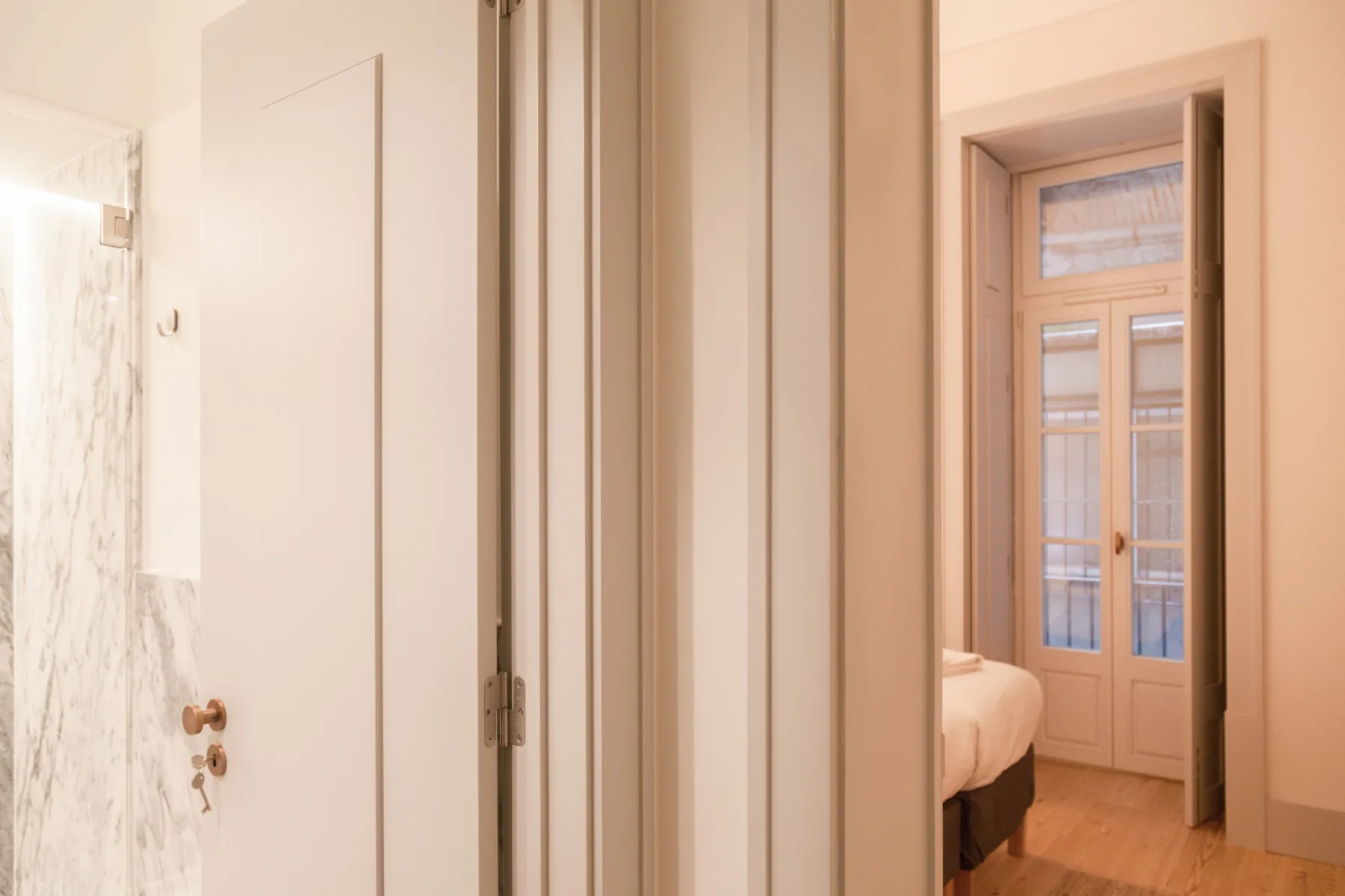 A bedroom is visible through the doorway, with a bed beside tall glazed doors.