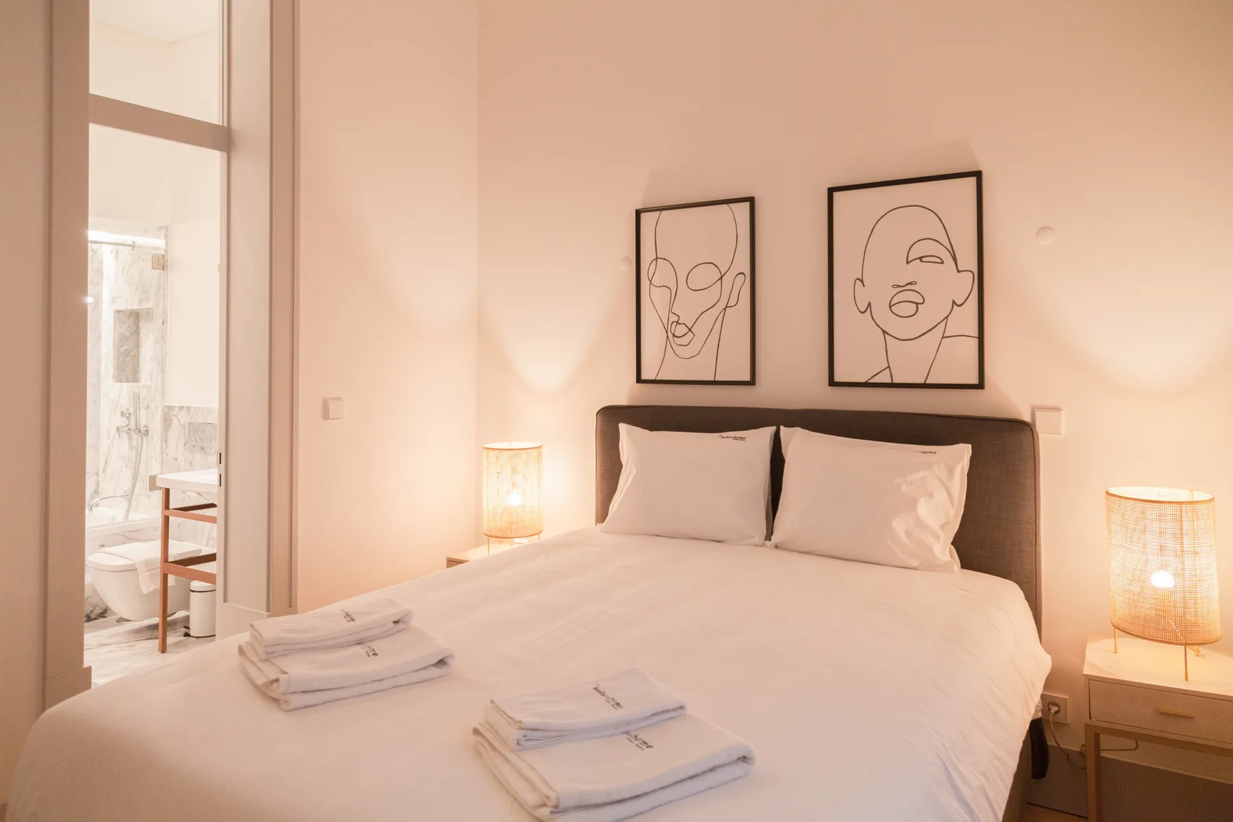 A bedroom with a neatly made bed and framed line drawings above the headboard.