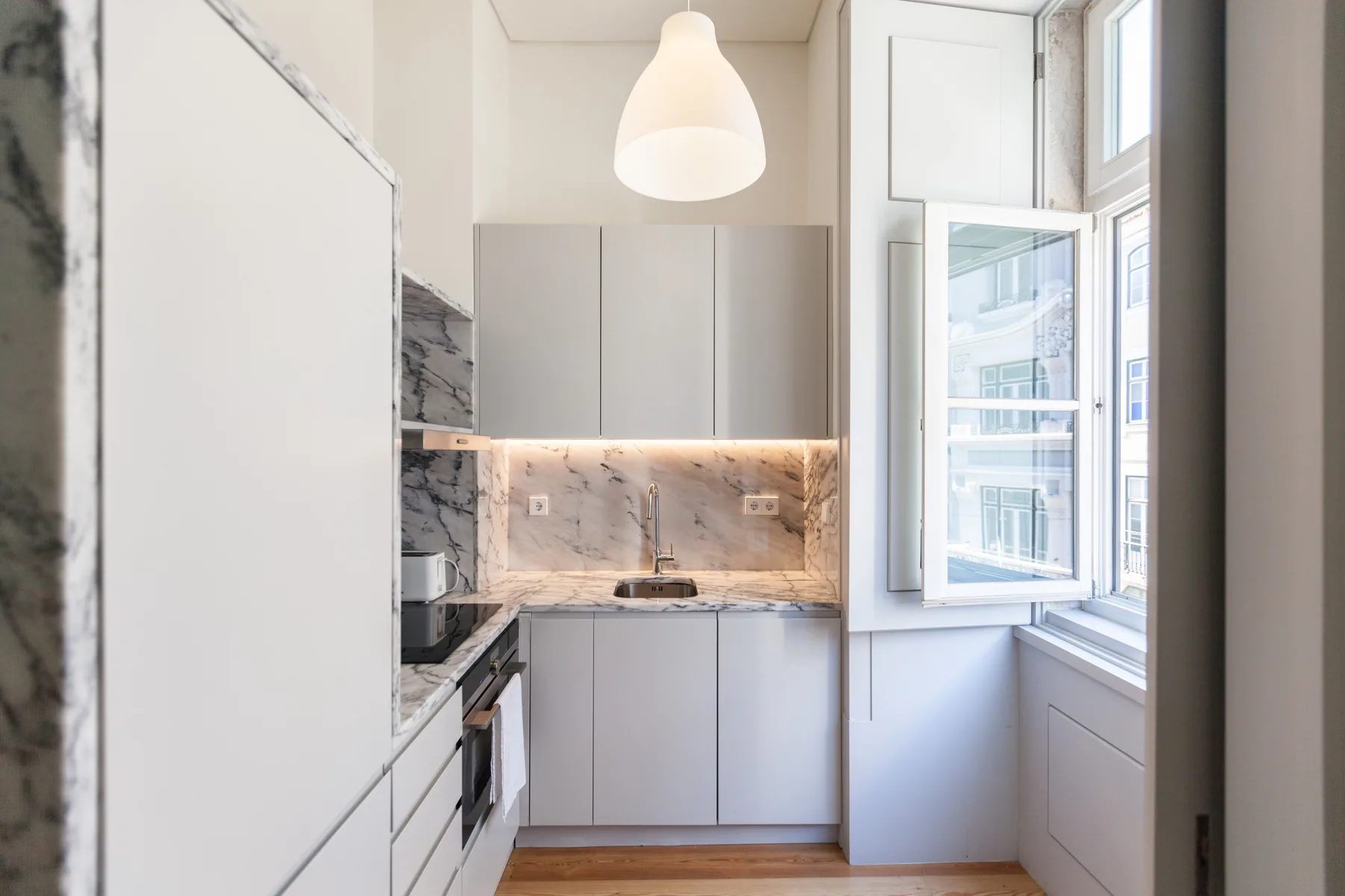 A compact kitchen with light cabinetry, marble-patterned surfaces, and a large window.