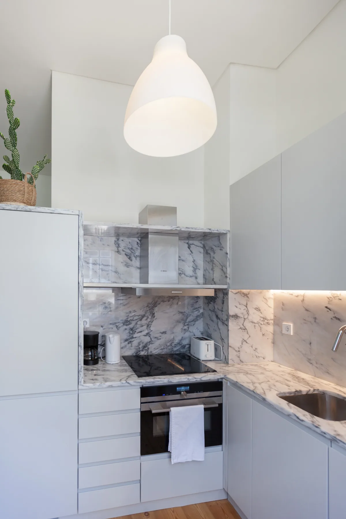 A modern kitchen with pale cabinetry, marble-patterned counters, and a hanging pendant light.