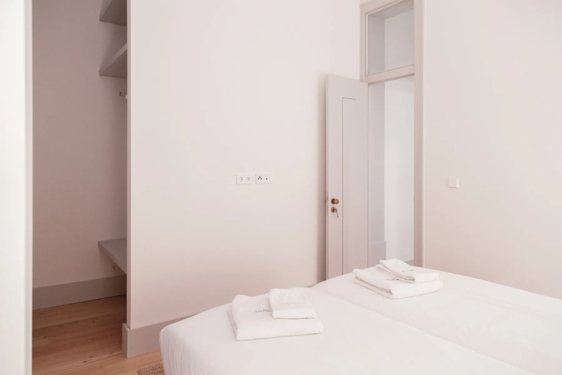 A bright bedroom with a neatly made bed and an open doorway.