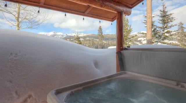 Una bañera de hidromasaje está bajo un patio cubierto, con montañas nevadas a lo lejos.