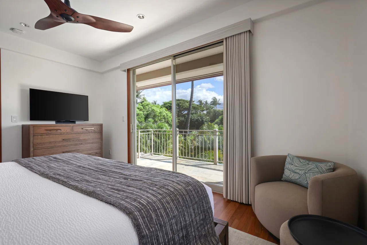 A bedroom with a bed, a television, and sliding glass doors opening onto a balcony.