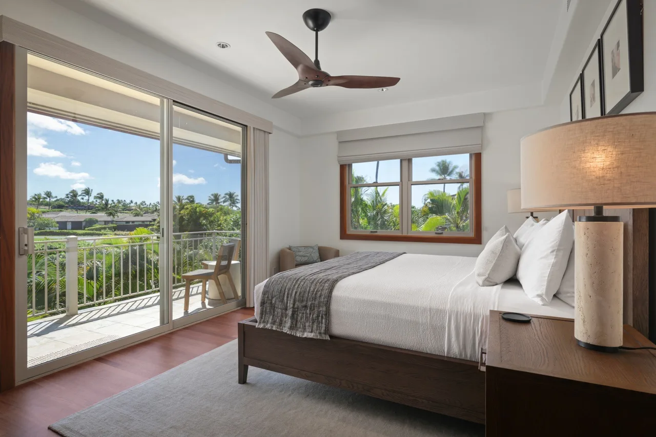 A bright bedroom with a large bed beside sliding glass doors opening onto a balcony.