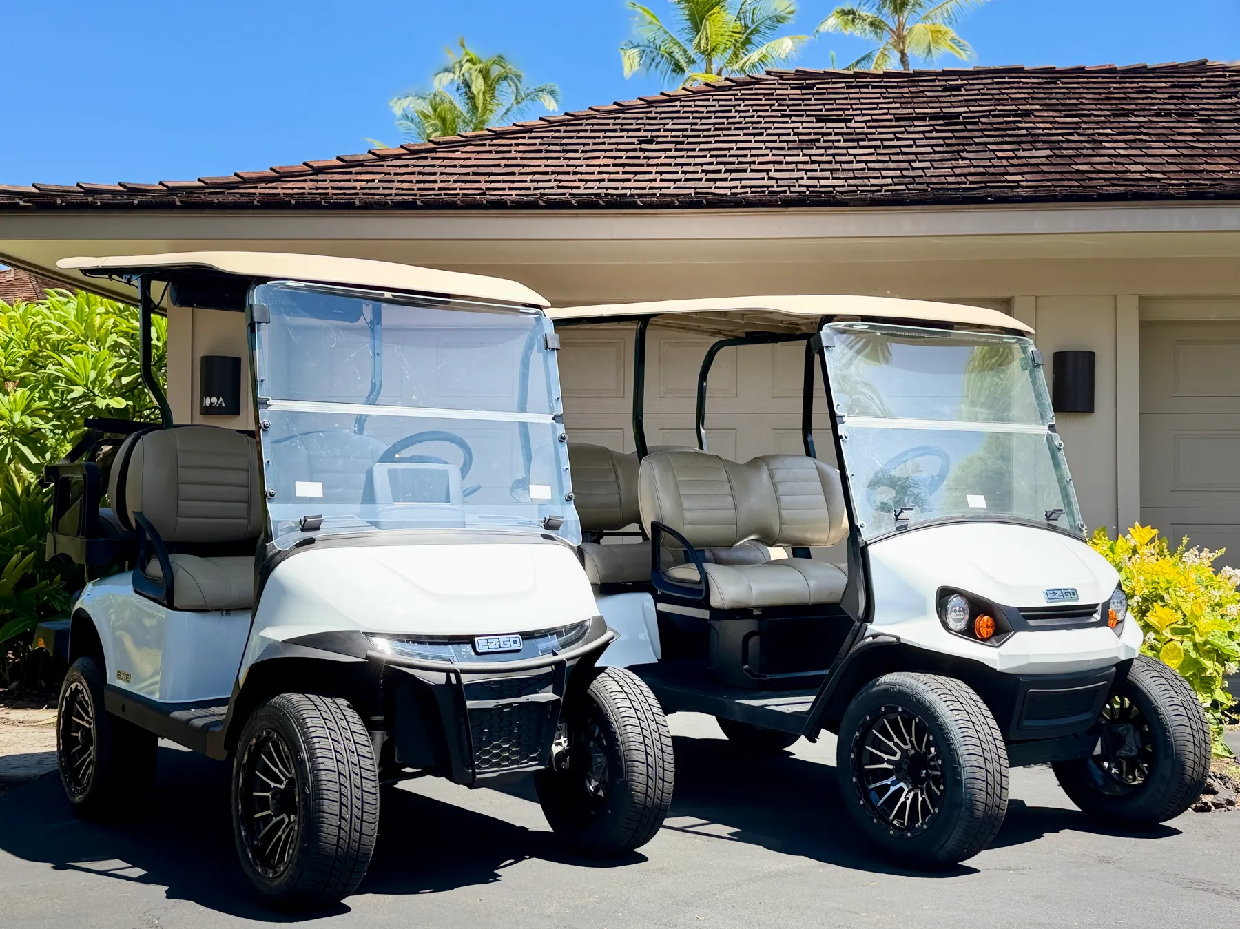 Two golf carts are parked outside a low building beneath a tiled roof.