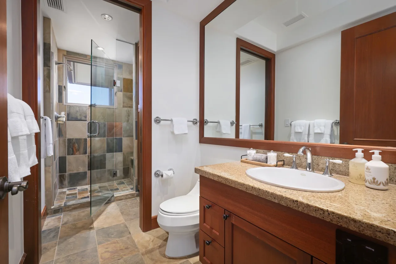 A bathroom with a vanity, sink, toilet, and glass shower.