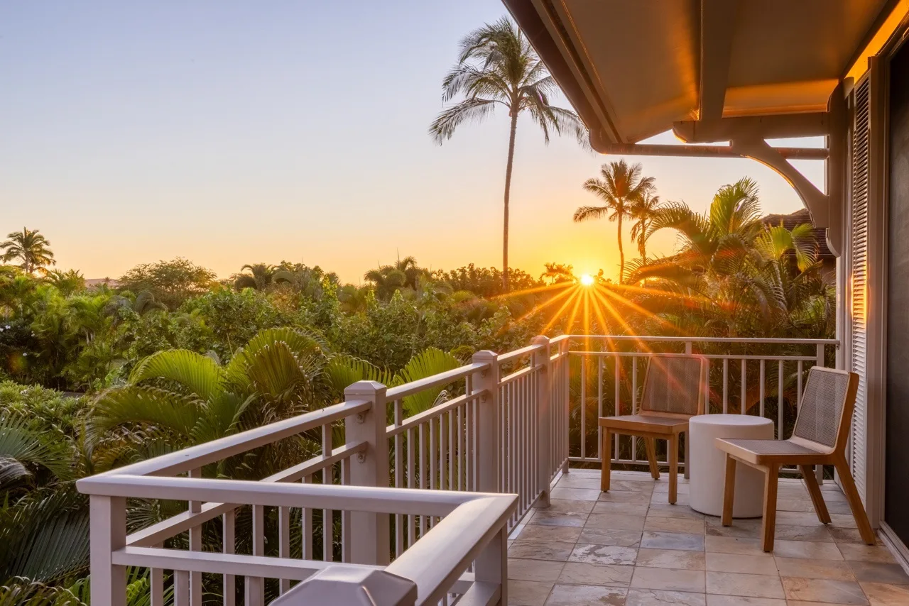 A tiled balcony overlooks tropical greenery and palm trees at sunset.