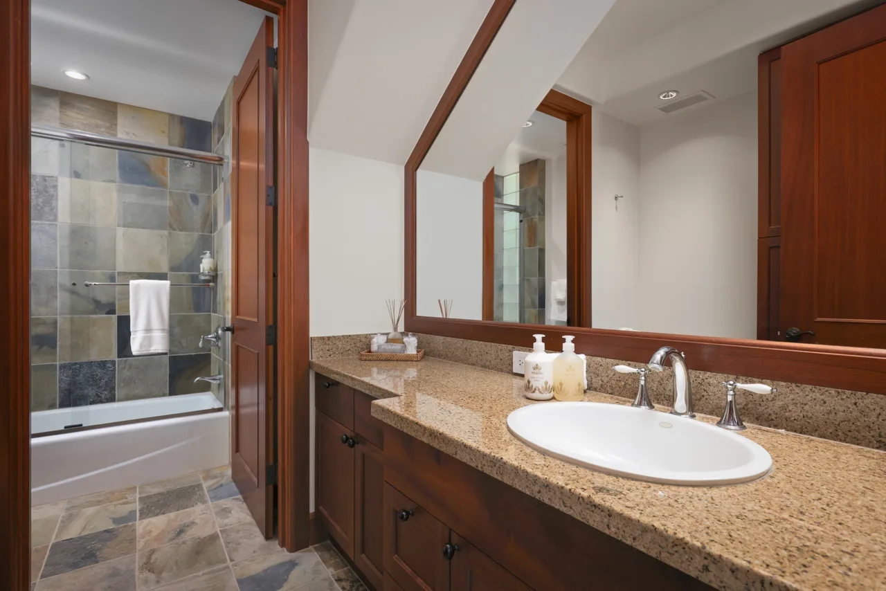 A bathroom vanity with a wide mirror and a tiled shower area.