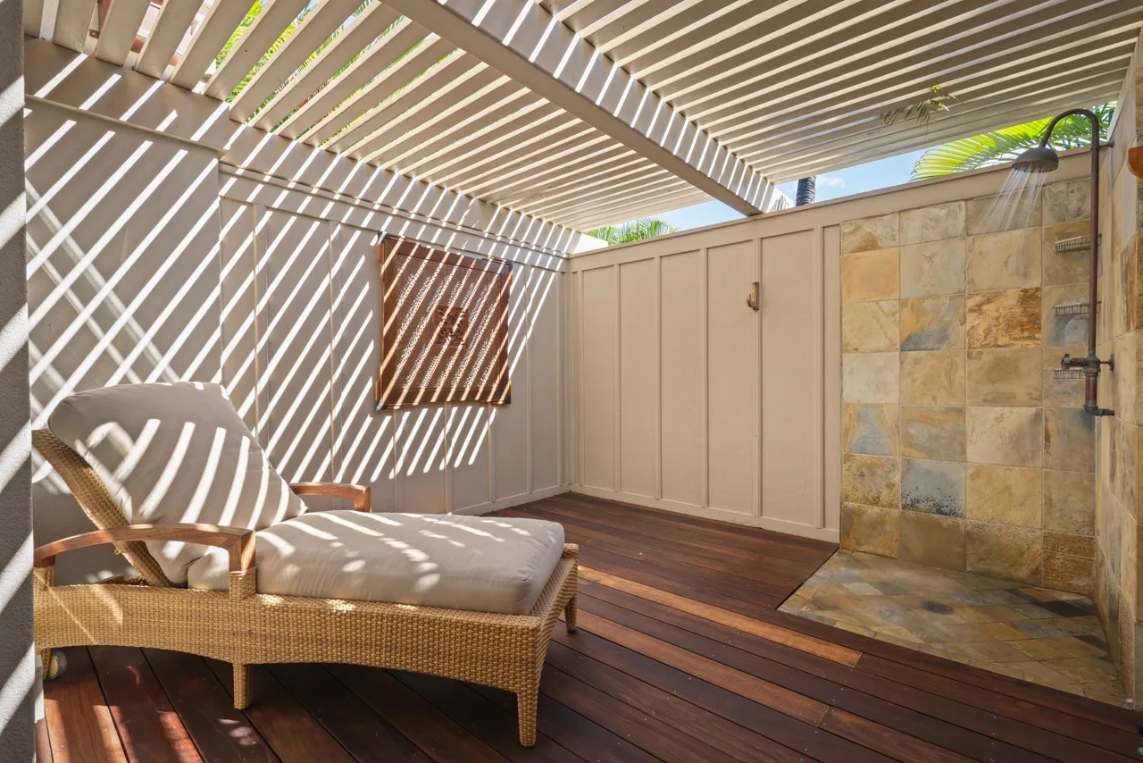 A shaded outdoor patio has cushioned seating and an open shower area.