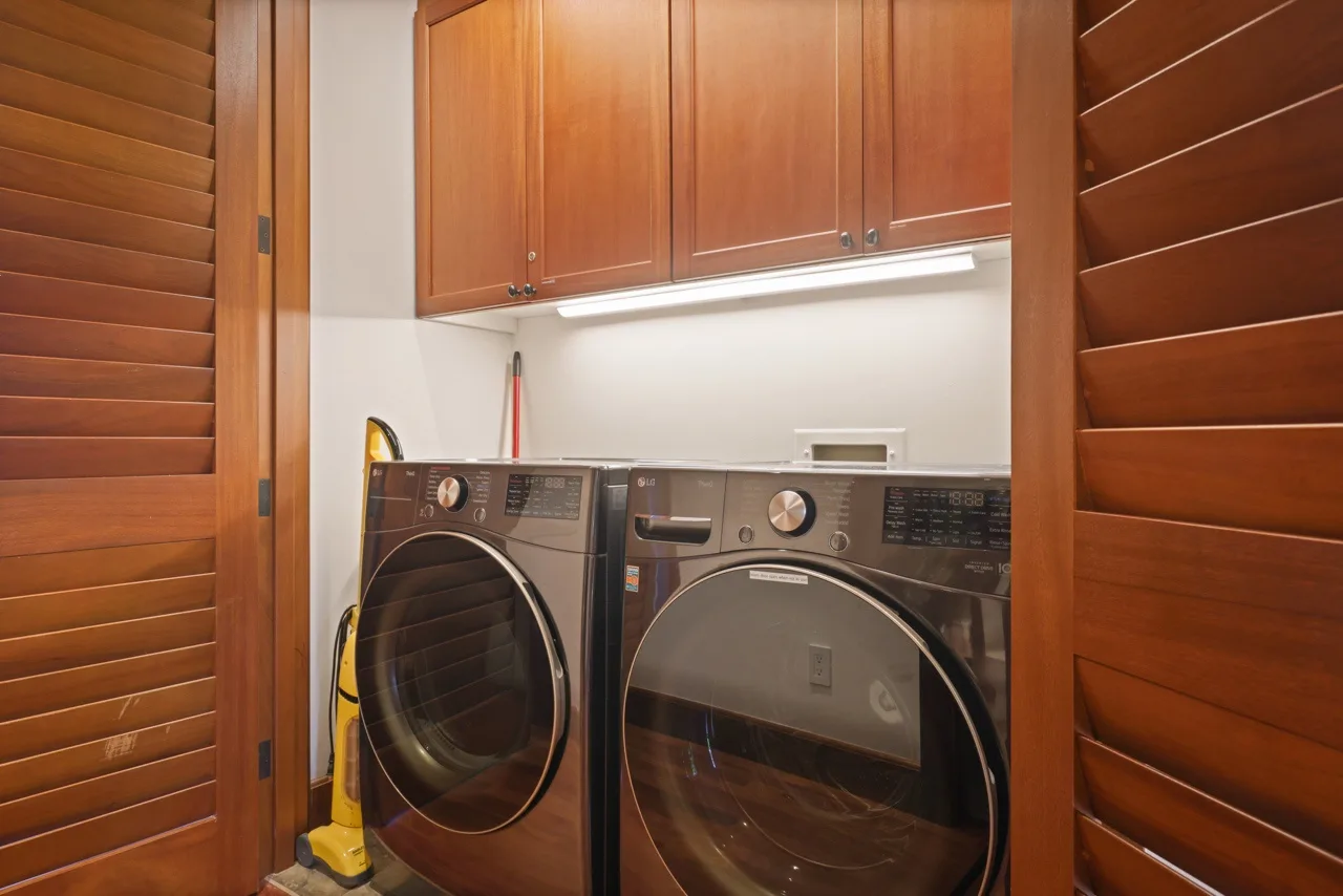 A laundry area with a front-loading washer and dryer beneath wooden cabinets.