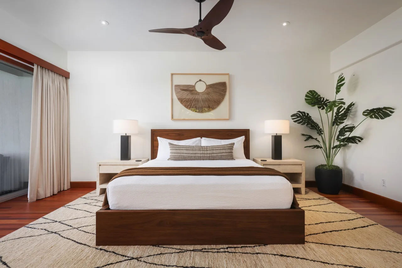 A bedroom with a neatly made bed, bedside lamps, and a potted plant.