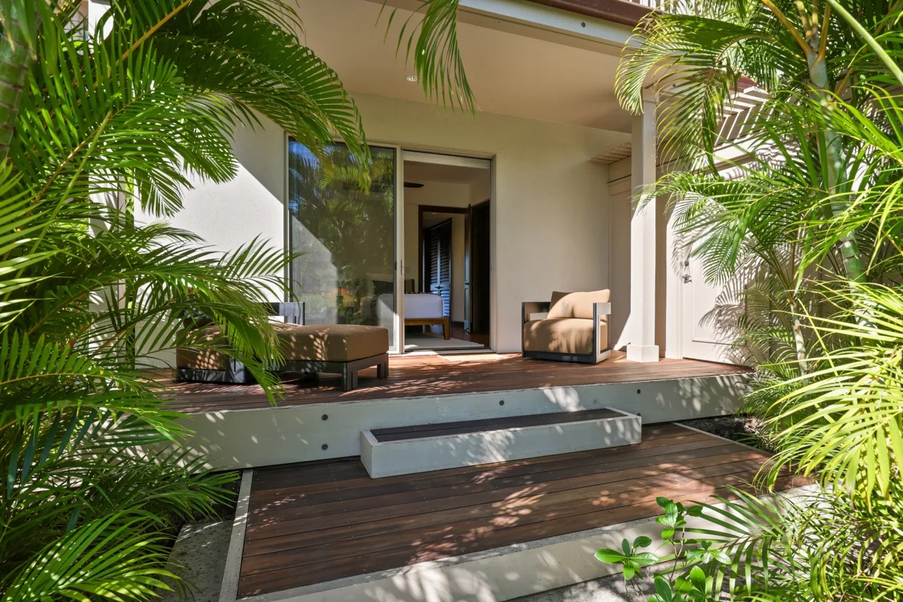 A covered patio with seating opens onto a garden framed by lush greenery.