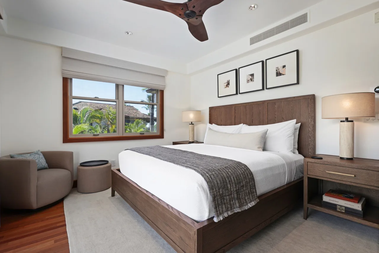 A bedroom with a neatly made bed, bedside lamps, and a window overlooking greenery.