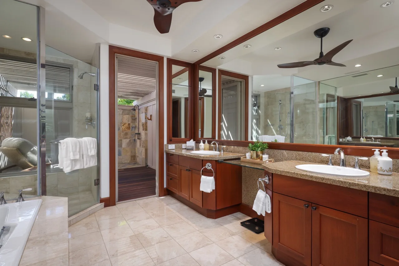 A spacious bathroom has wood vanities, large mirrors, and a glass-enclosed shower.
