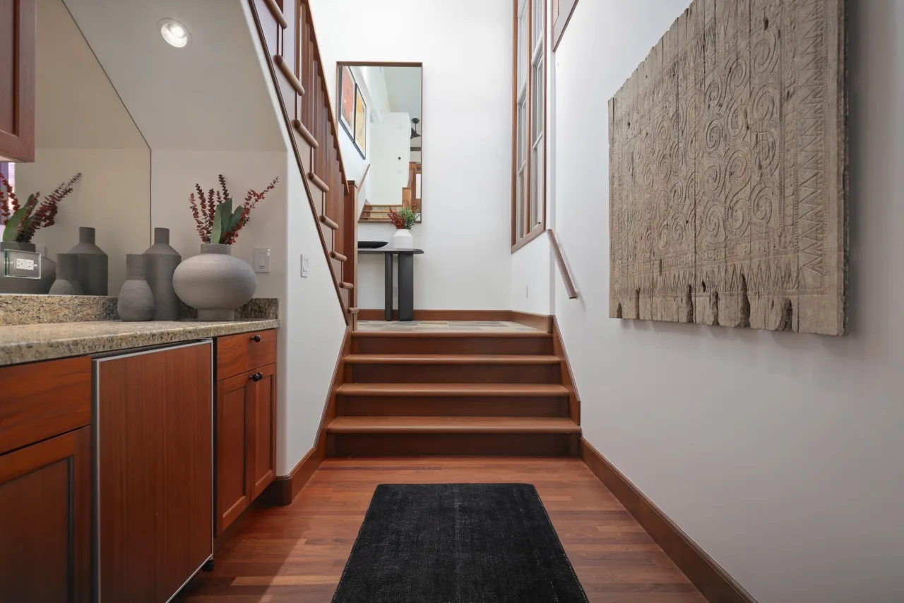A narrow interior hallway with wooden stairs and a long dark rug.