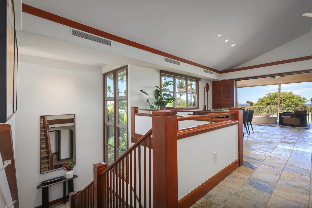 A bright open interior with a wooden staircase railing and large windows overlooking greenery.