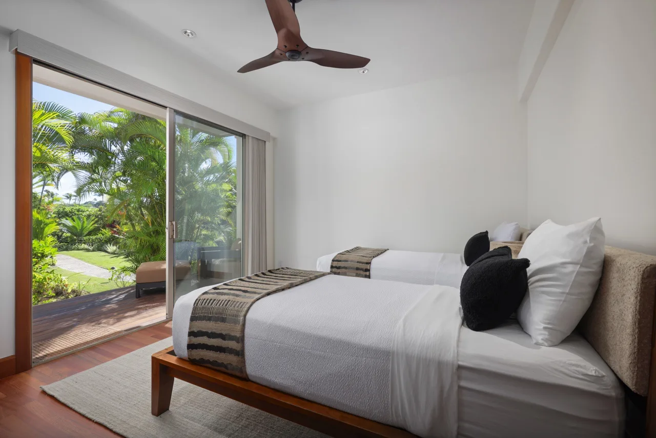 A bedroom with white bedding and sliding glass doors opening onto a garden.
