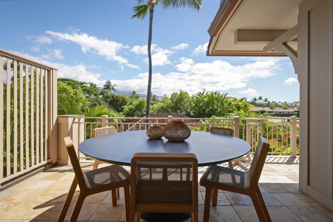 An outdoor dining area with a round table and seating overlooks a leafy landscape.