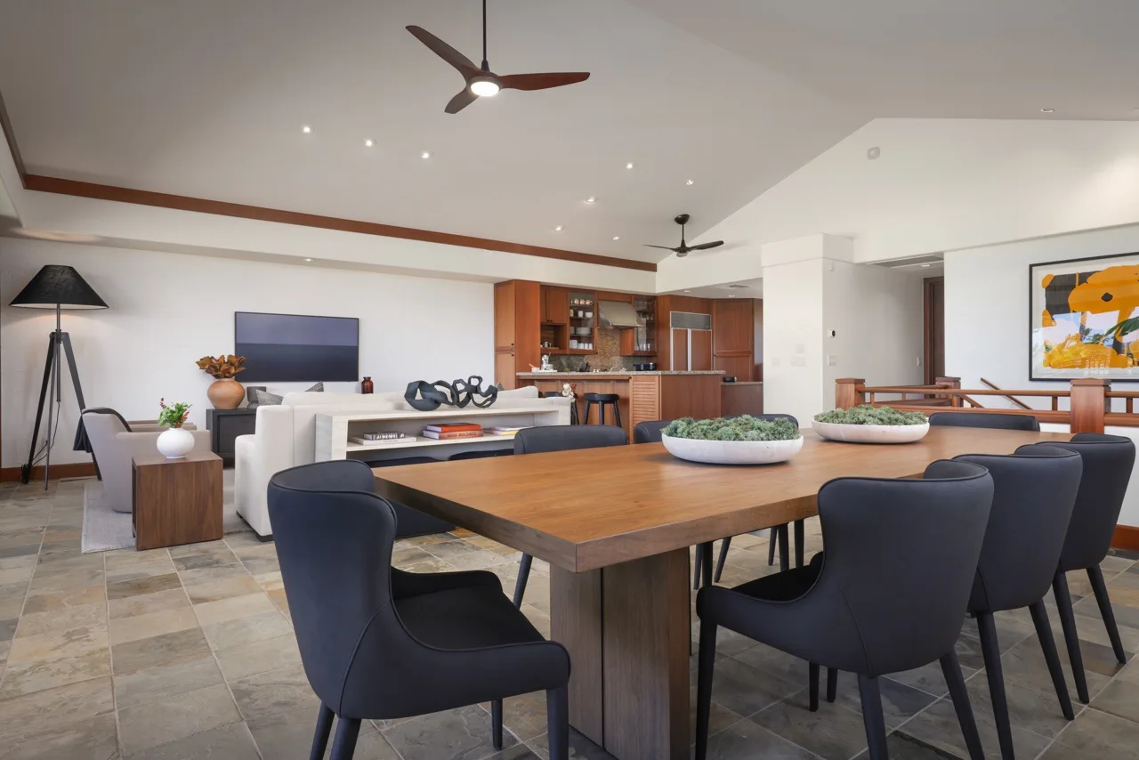A dining and living area with a large wooden table and dark seating.