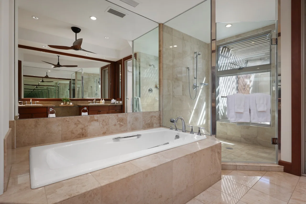 A spacious bathroom with a built-in bathtub, glass shower, and large mirrors.