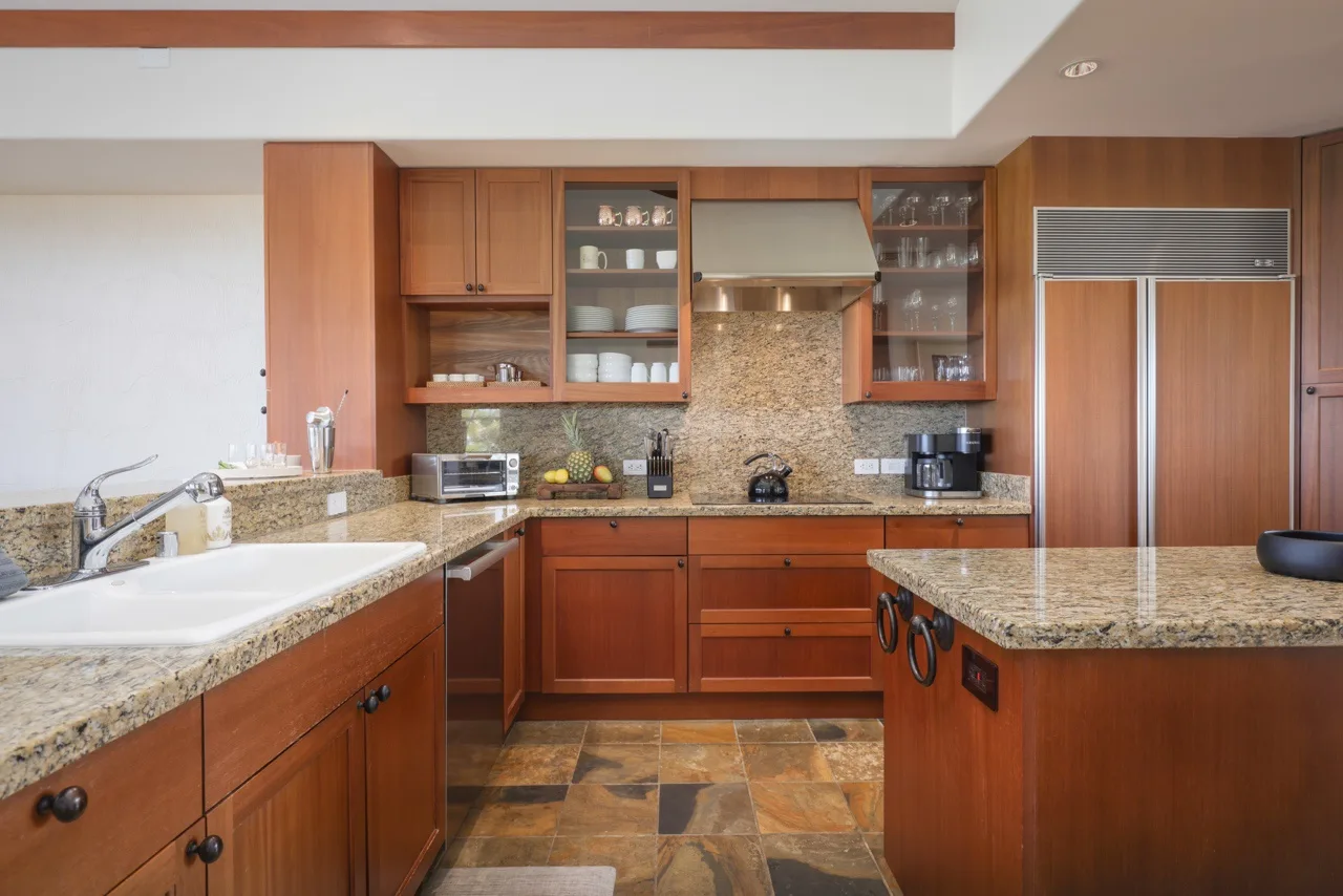 A kitchen with wooden cabinets, stone countertops, and stainless steel appliances.