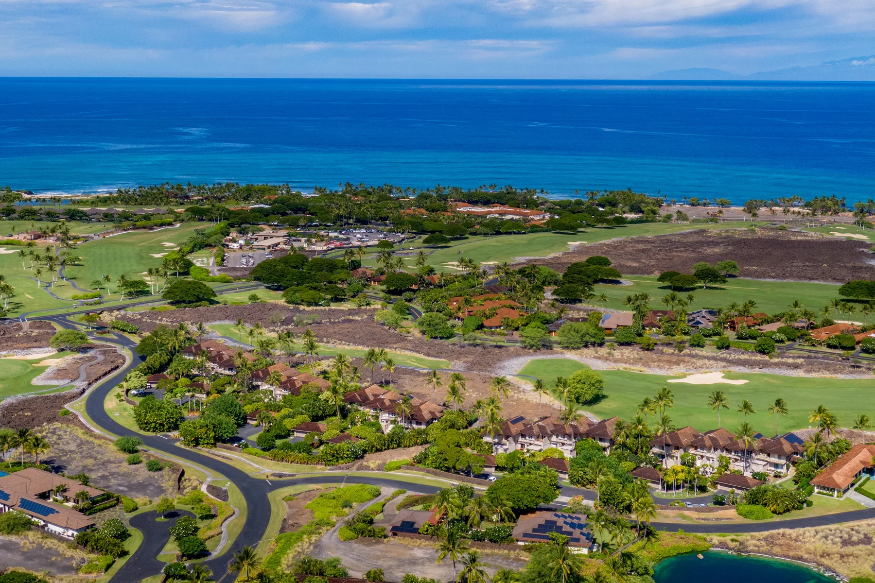 Aerial view of a coastal landscape with green fields and the ocean beyond.