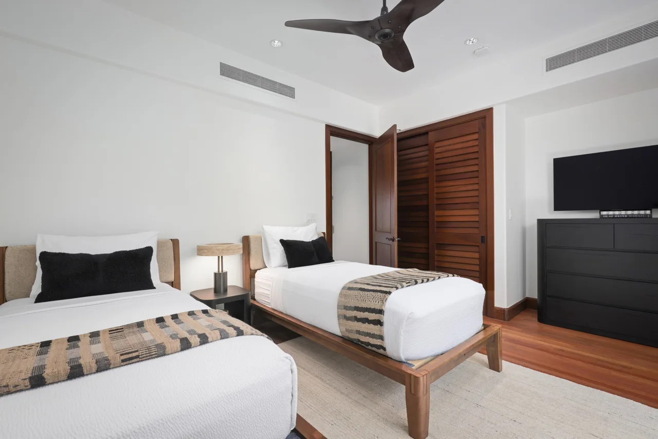 A bedroom with two beds, wooden flooring, and a ceiling fan.