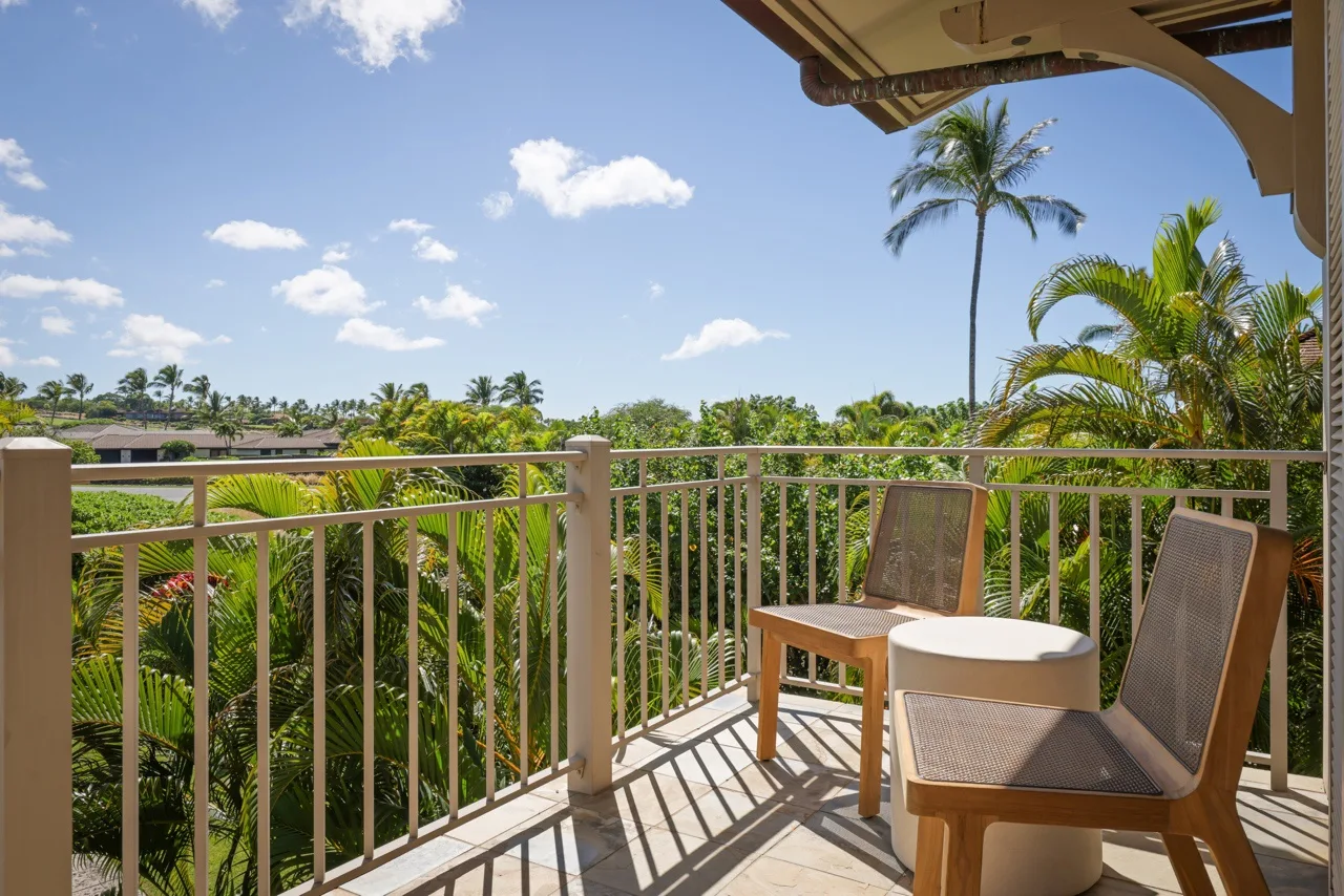 A balcony with outdoor seating overlooks palm trees and green foliage.