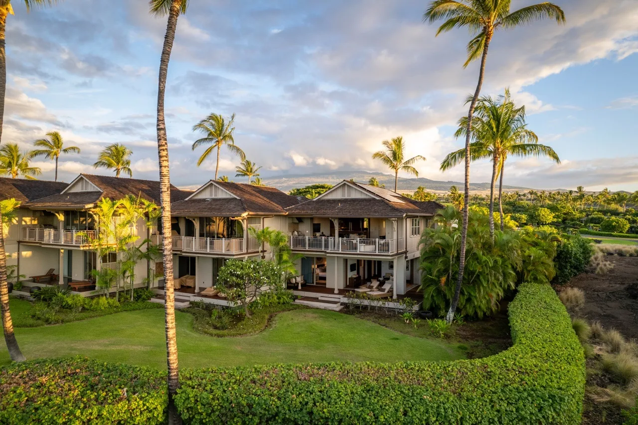 A tropical residential complex with balconies and palm trees around a landscaped lawn.