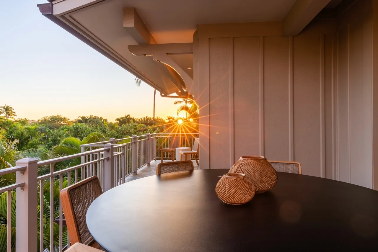 A covered balcony seating area overlooks green trees in the sunset light.