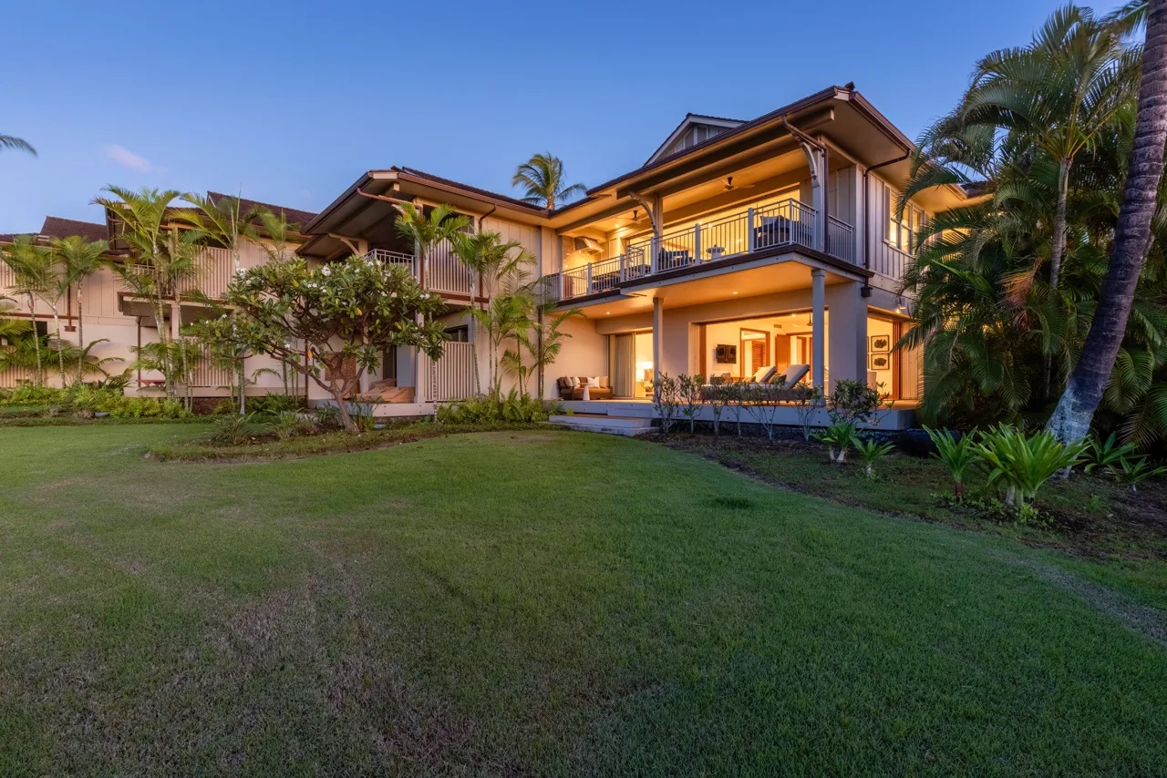 A two-story house with a balcony stands beside a broad green lawn.